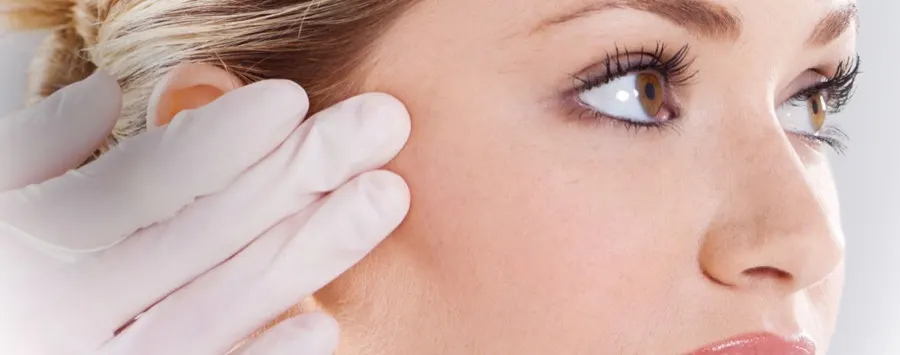 A gloved hand beside a patient&rsquo;s face during a cosmetic consultation